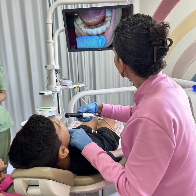 Dentista usando a câmera na boca do menino, com a imagem aparecendo na tela