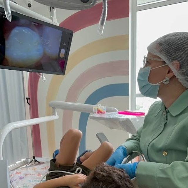Criança deitada na cadeira com o dente ampliado na tela ao lado