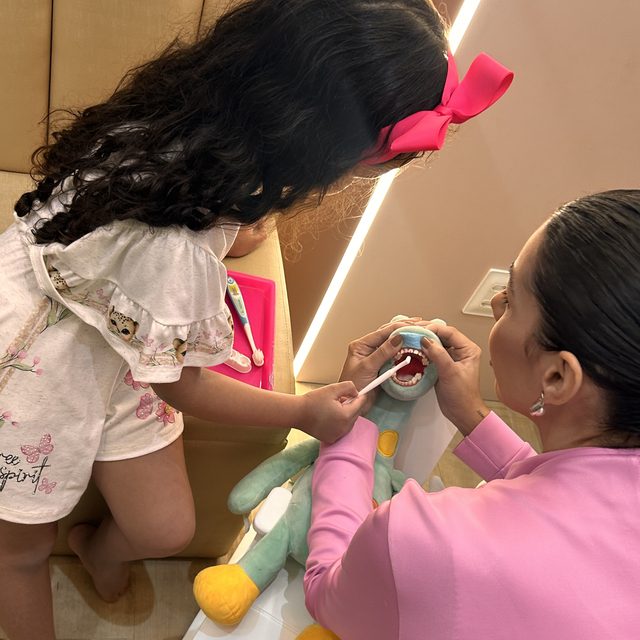 Criança escovando os dentes do bicho de pelúcia com a dentista