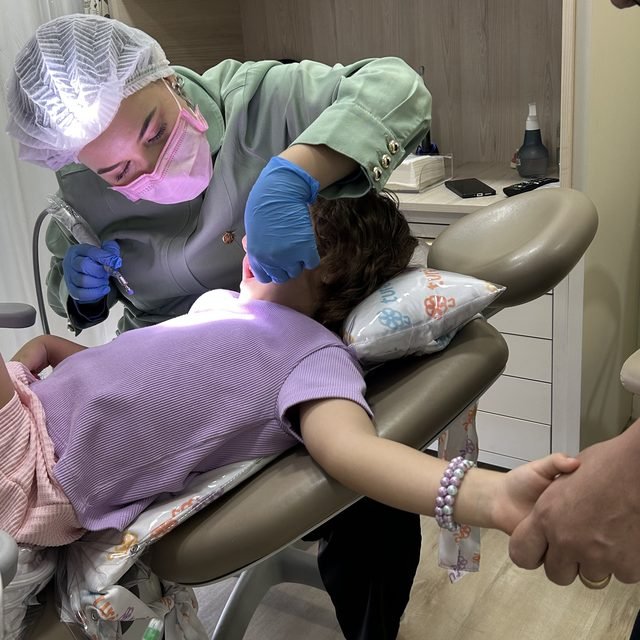 Menina segurando a mão de um adulto enquanto a dentista atende