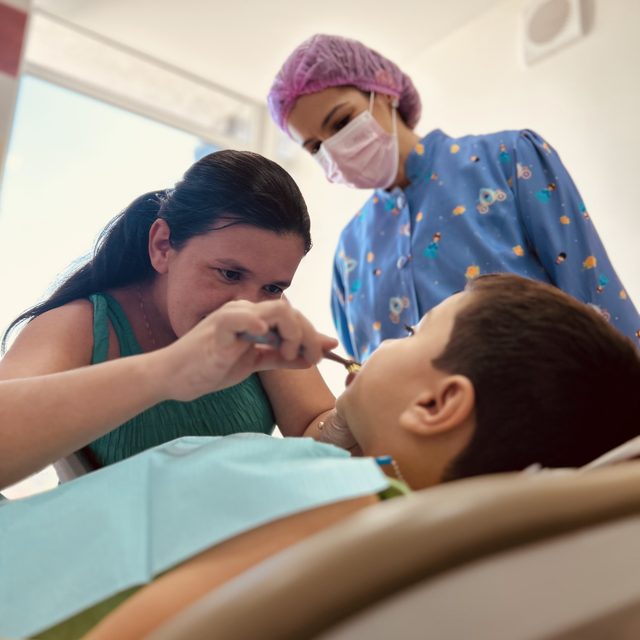 Mãe escovando os dentes do filho enquanto a dentista observa